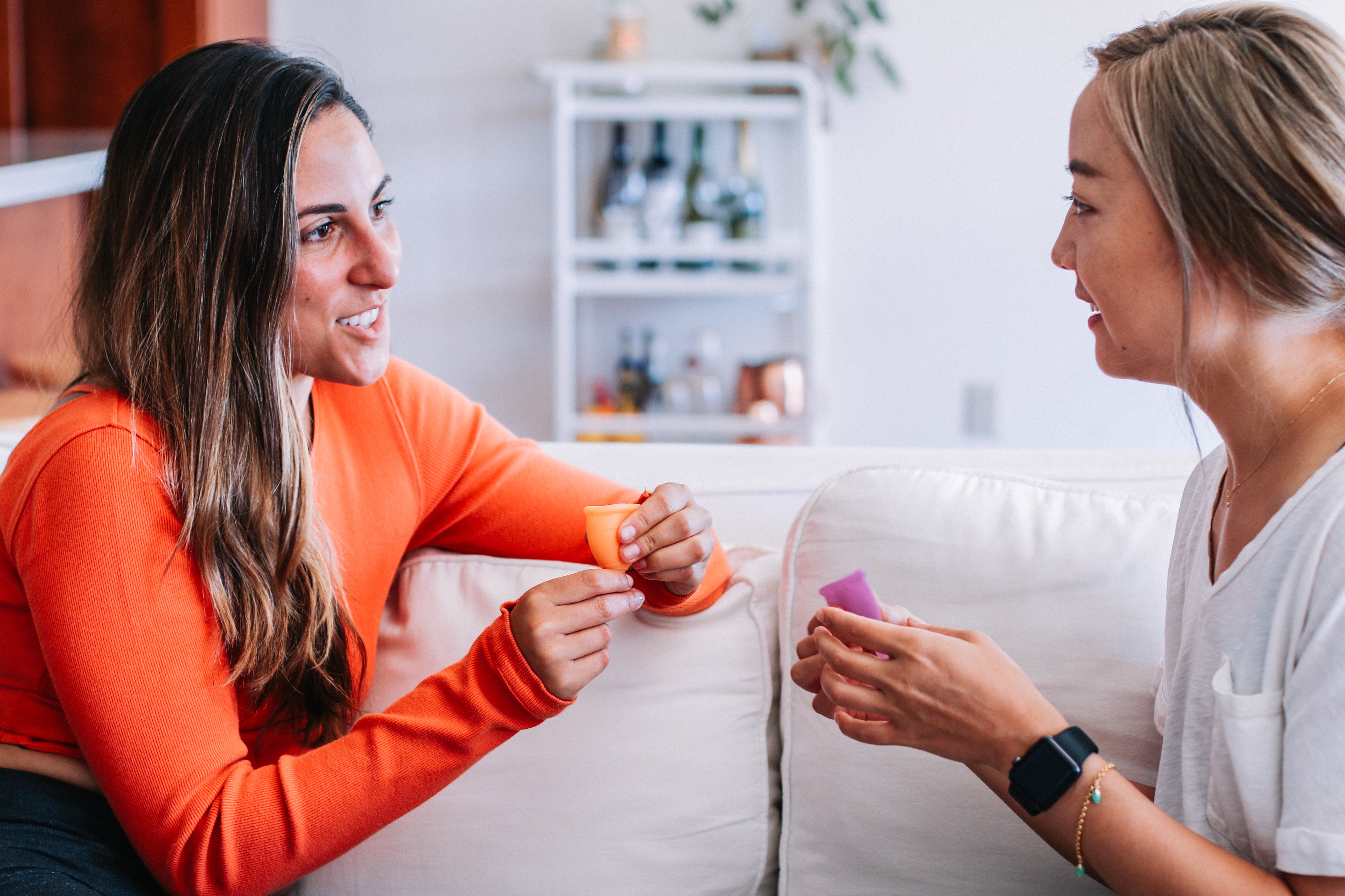 Photograph of two friends chatting. Each has a menstrual cup in their hands.