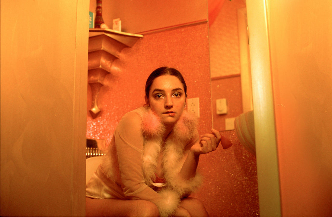 Photograph of a young lady sitting on the toilet, holding a menstrual cup in her left hand.